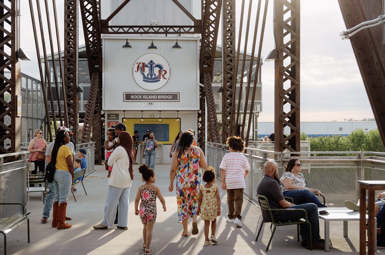 Visitors walking, gathering and sitting beneath the steel trusses at Rock Island Bridge, with the venue entrance in view